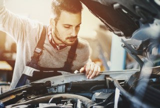 Closeup of mechanic in engine bay, preparing a car for the summer season.