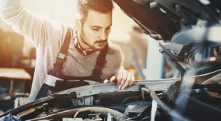Closeup of mechanic in engine bay, preparing a car for the summer season.